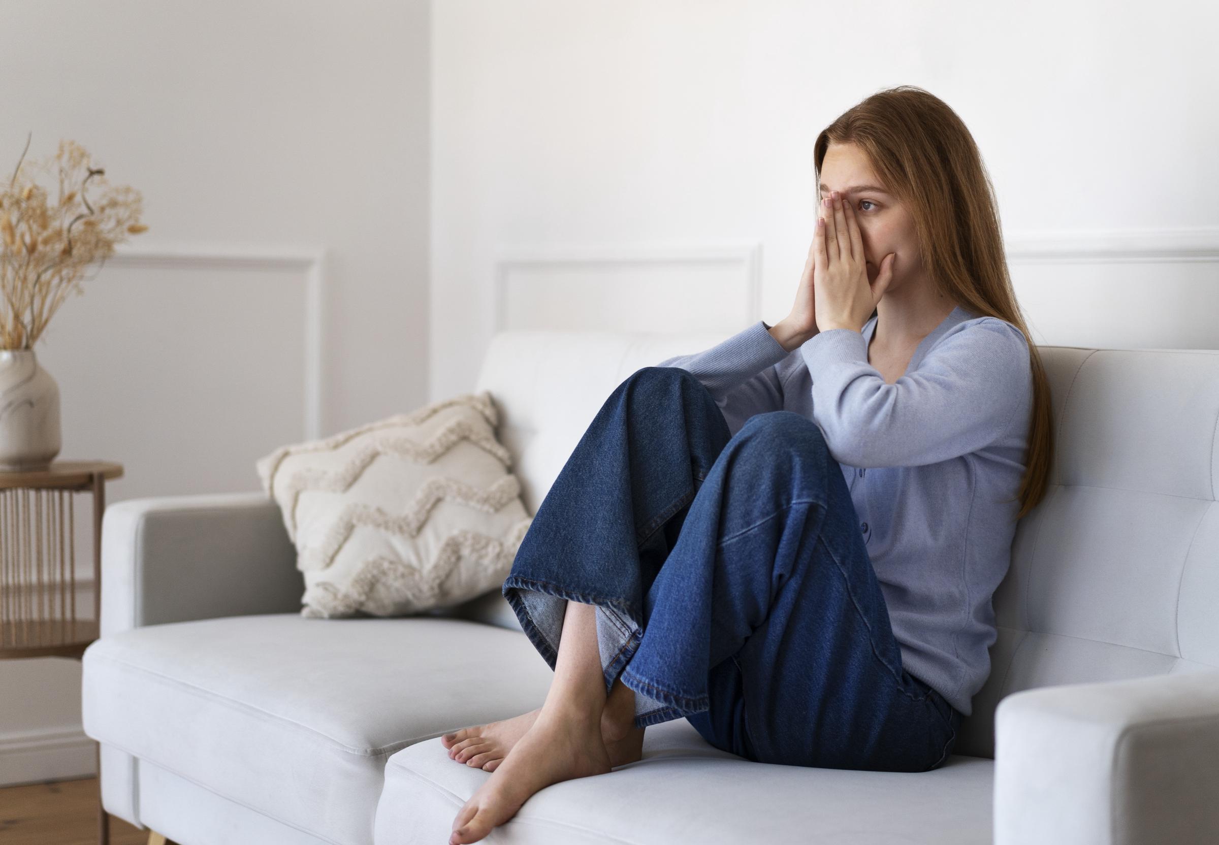 A worried woman sitting on a couch | Source: Freepik