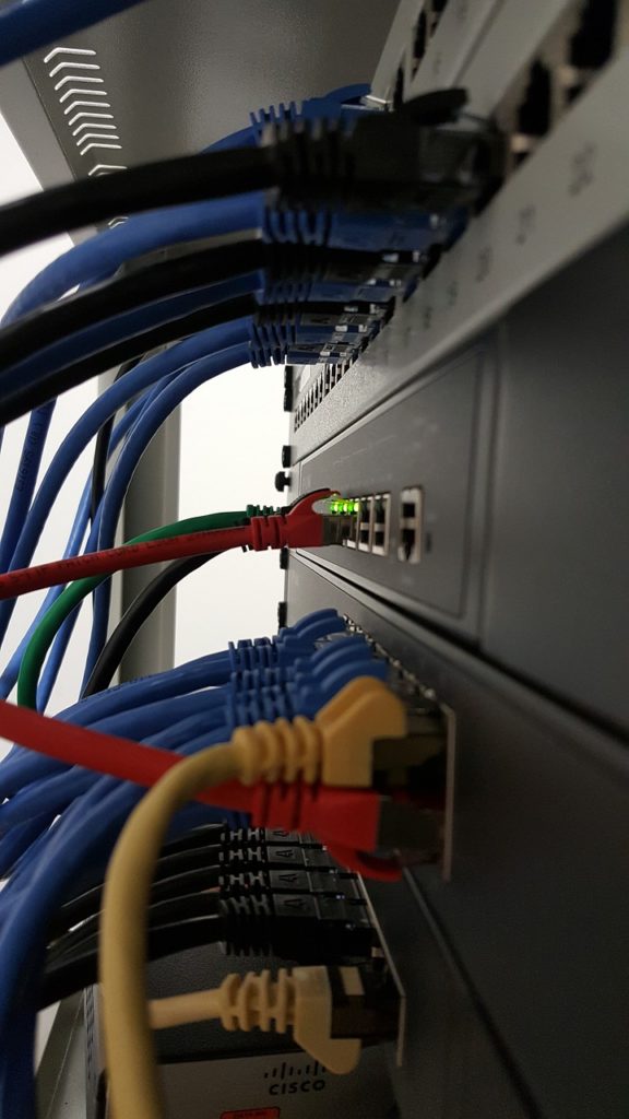 The back of a computer with numerous red, blue, yellow, and black cables plugged in. 