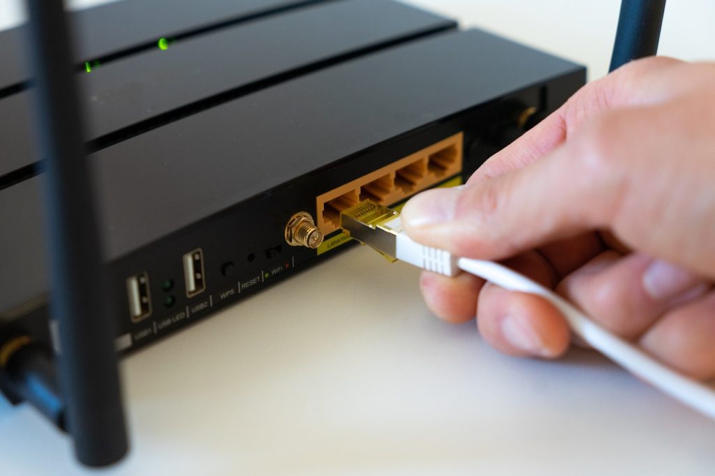 A hand plugging a cable into an internet router. White background. 